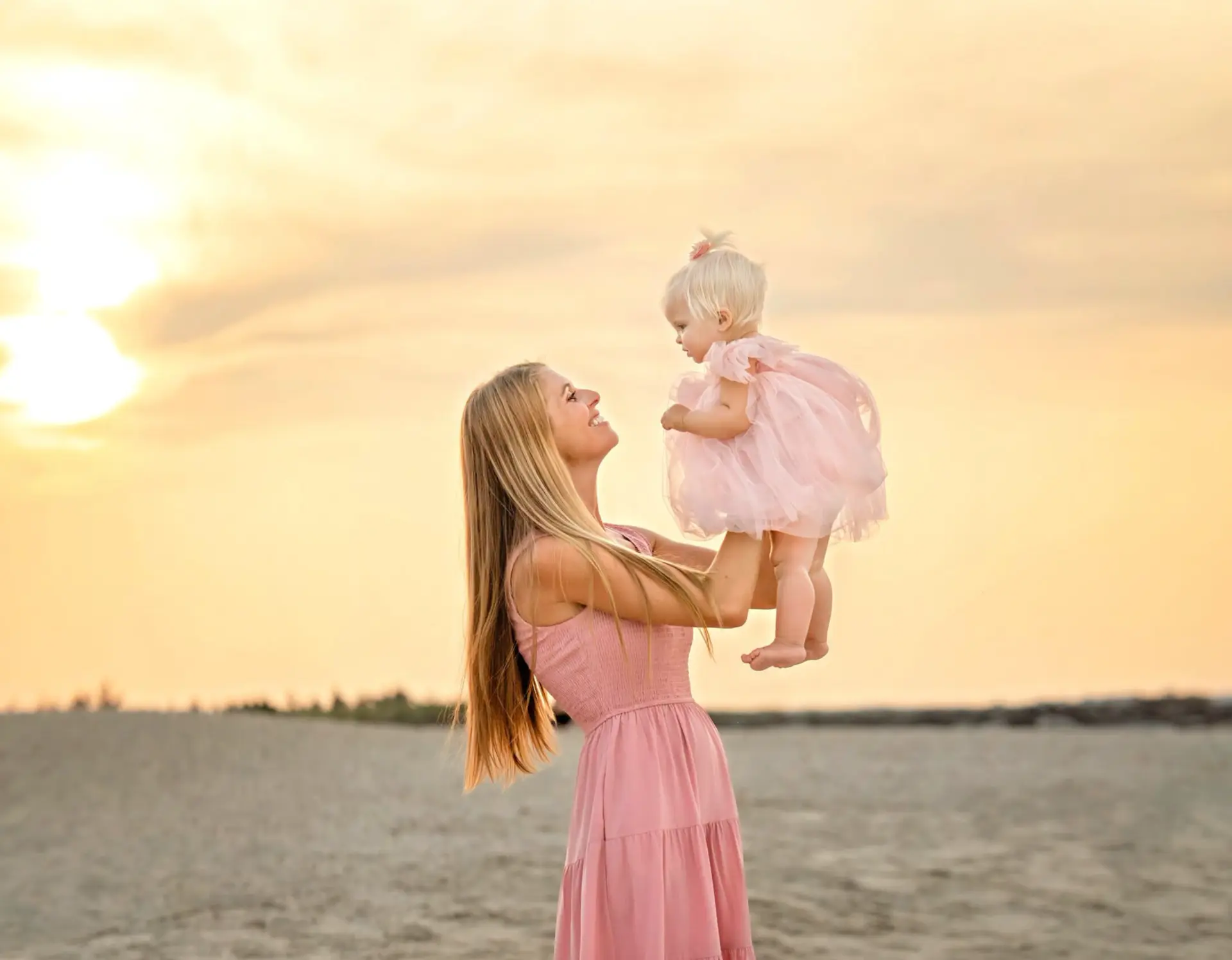 Mother lifting her baby at sunset