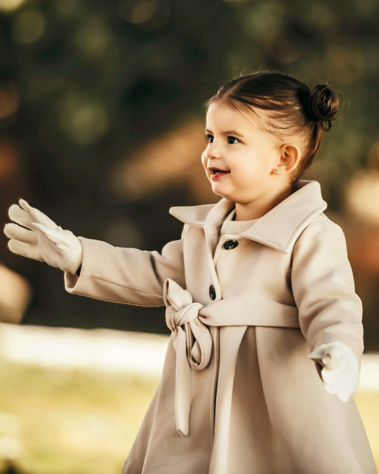 A toddler in a cream trench coat smiles in warm autumn light during a mini session portrait.